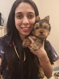 Dra. Ana Carolina segurando um cachorro em atendimento domiciliar, transmitindo cuidado e atenção.